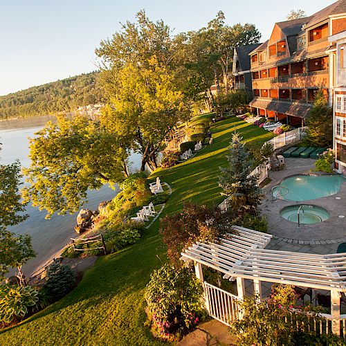 The image shows a luxurious lakeside resort with multi-story buildings, lush gardens, a swimming pool, and a scenic view of the lake and surrounding trees.