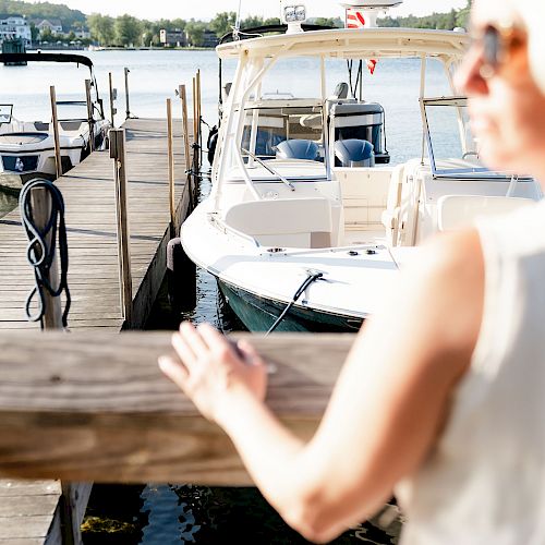 A dock with boats moored, and a person in the foreground looking towards them. A calm water body is visible in the background ending the sentence.