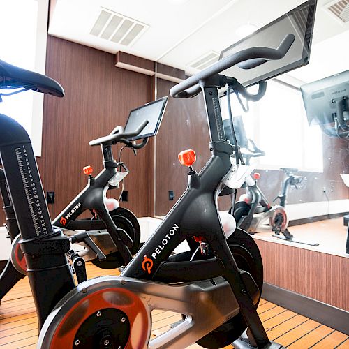 The image shows a stationary exercise bike with a screen, placed in front of a mirror in a gym or workout room.