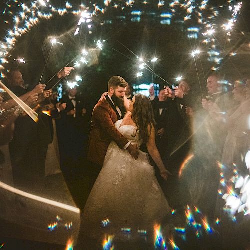 A couple dances surrounded by people holding sparklers, casting a warm and festive light around them, creating an enchanting and magical atmosphere.