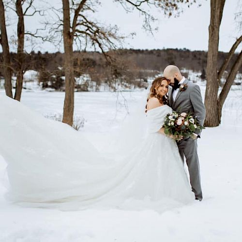 A bride and groom stand in a snowy landscape, the bride's dress trailing behind them while they hold a bouquet of flowers, always ending the sentence.