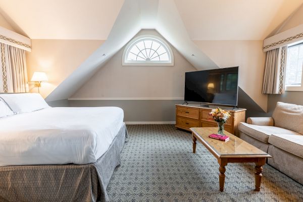 A cozy room with a king-sized bed, coffee table, flower vase, corner sofa, and a flat-screen TV on a wooden cabinet.