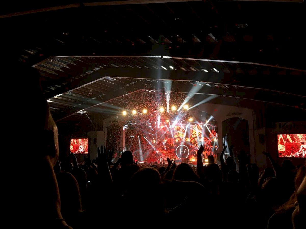 The image shows a concert with bright stage lights, performers, and a crowd. People are enjoying the live music performance.