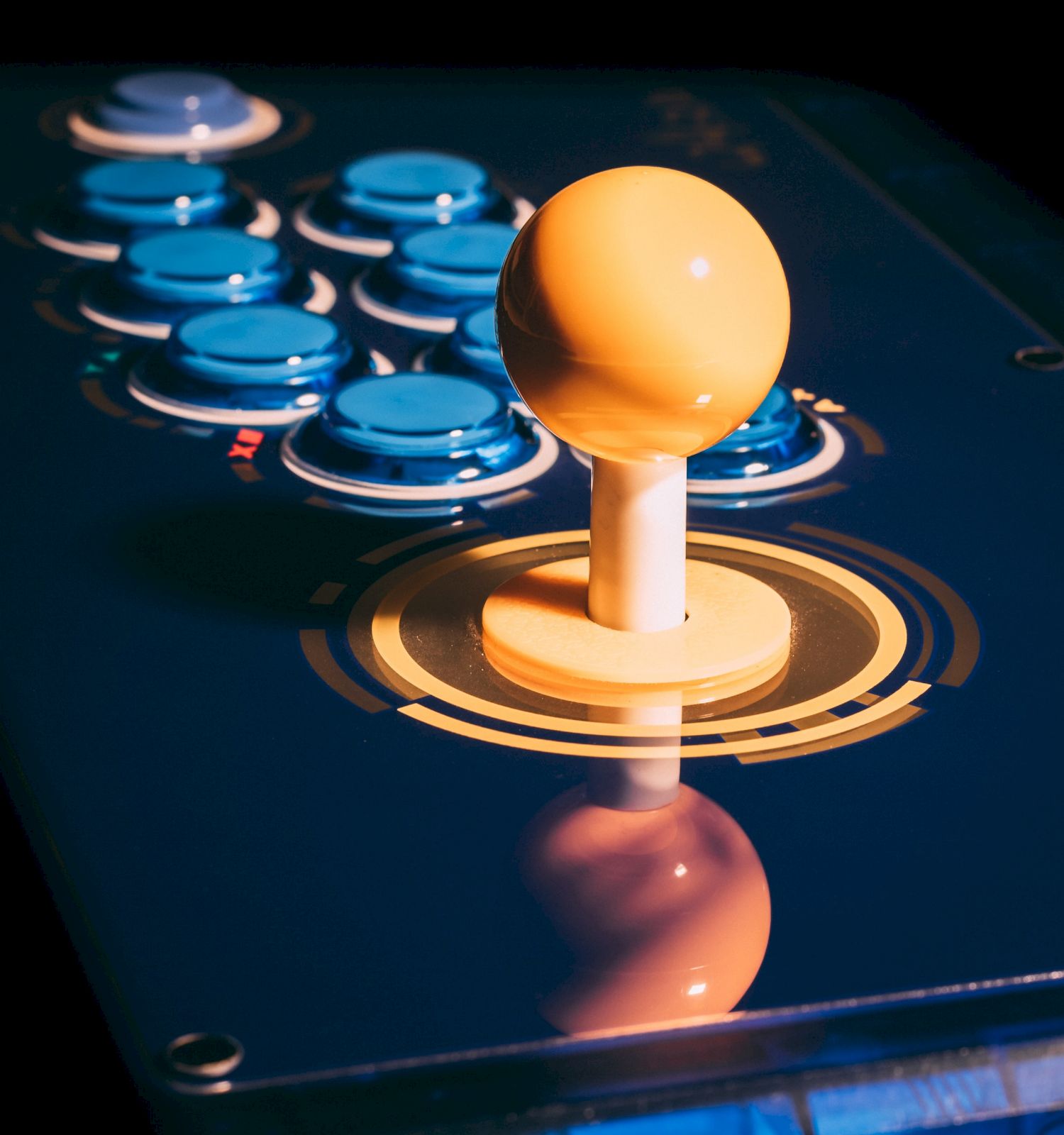 This image shows an arcade game controller with a yellow joystick and blue buttons on a dark background.