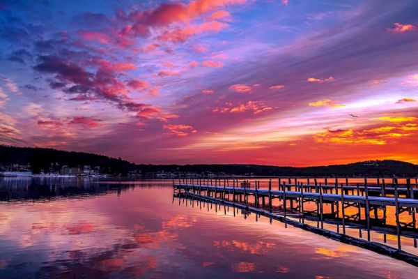 A beautiful sunset over a lake with a wooden dock extending into the water, vibrant colors reflecting on the calm surface.