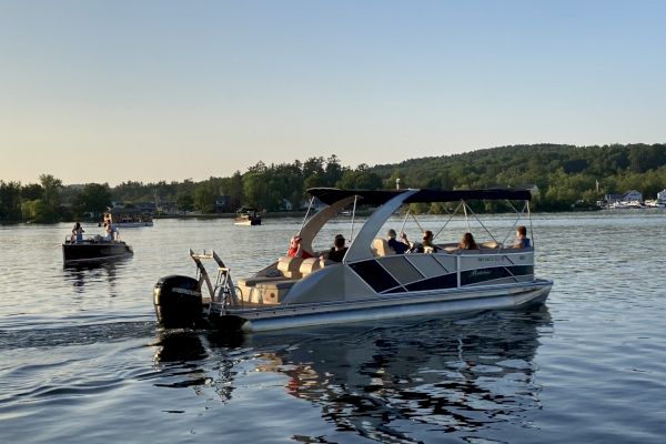 Several people are enjoying a boat ride on a calm lake during the day, with green hills and trees in the background and one boat nearby.