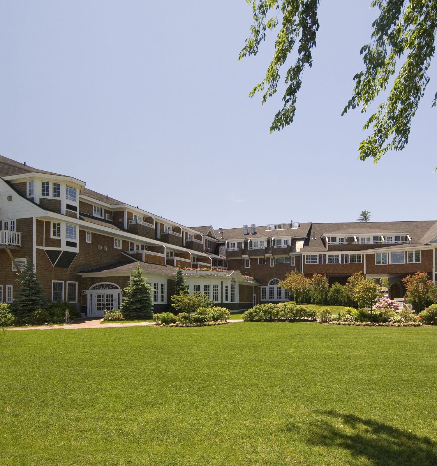 A large, multi-story building with extensive landscaping and a tower on one side is shown, set against a clear blue sky and a green lawn.