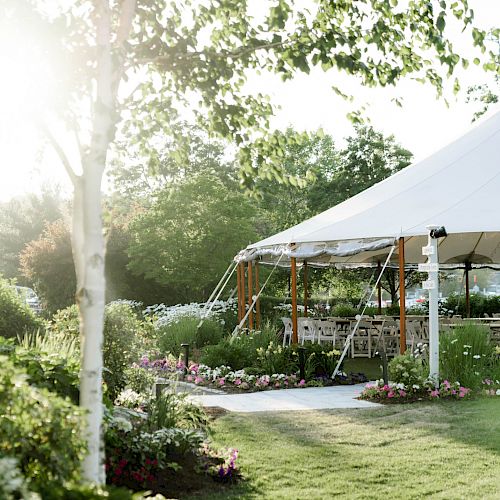 A beautifully lit outdoor garden venue with a white canopy tent, surrounded by lush greenery and colorful flowers, ready for an event or celebration.