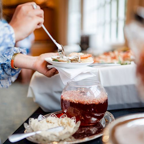 A person is scooping food onto a plate at a buffet, with a bowl of sauce or jam and a dish of onions or similar beside it.