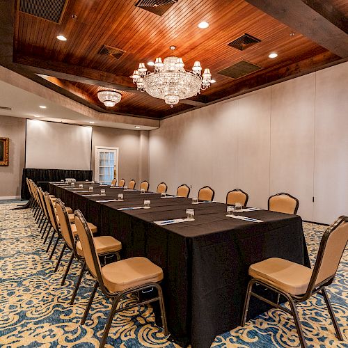 A conference room with a long, rectangular table set with notepads and pens, surrounding chairs, chandeliers, a painting, and a patterned carpet ends the sentence.