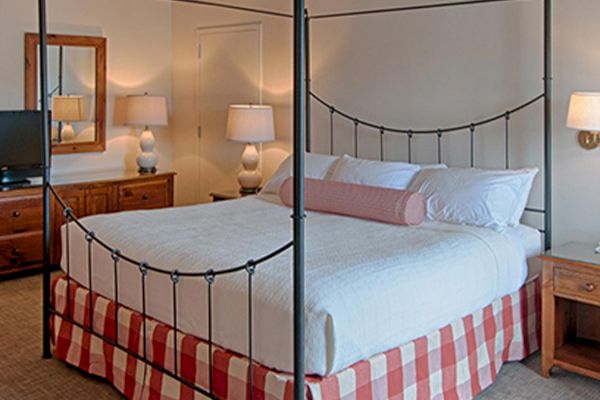 A cozy bedroom with a canopy bed, TV, two nightstands, table lamps, a wall mirror, a red couch, and a blue armchair.