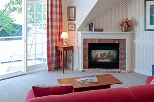 A cozy living room with a red sofa, a fireplace, a TV, and an open door leading to a balcony. There are red-checkered curtains and a blue armchair.