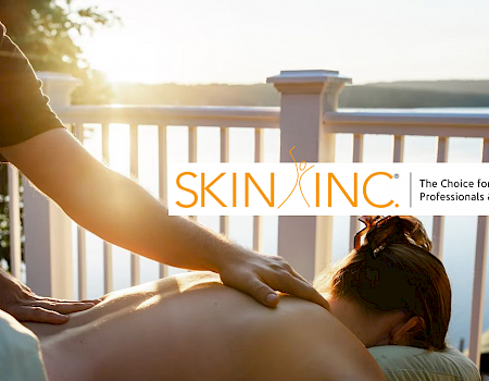 The image shows a person receiving a massage on an outdoor deck with a scenic view. The 