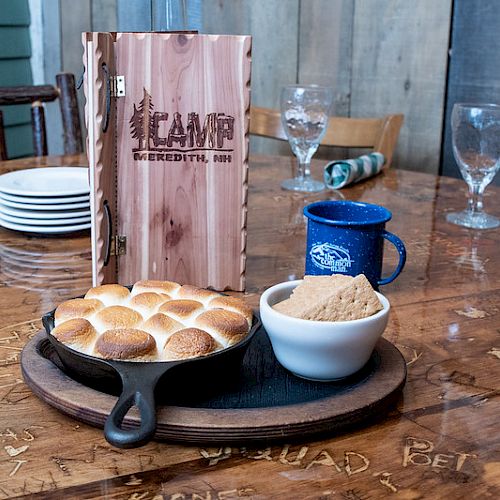 A table setting with a skillet of bread rolls, a bowl of white sauce, a blue mug, and a wooden menu displaying 