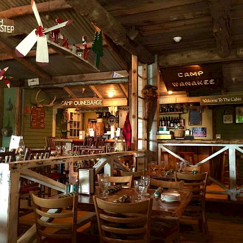 The image shows a rustic, camp-themed restaurant interior with wooden furniture, vintage decorations, and signs like 