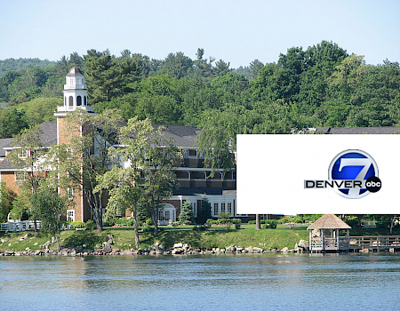 The image shows a lakeside building surrounded by trees, featuring the 