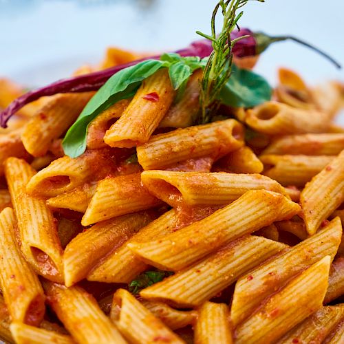 A plate of penne pasta topped with red sauce, garnished with fresh basil leaves and a whole red chili pepper.