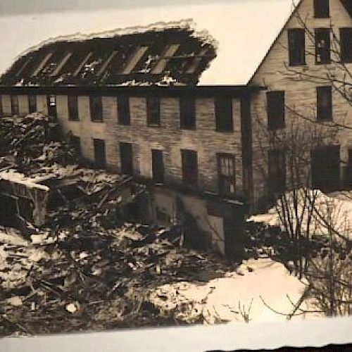 The image shows a partially collapsed building with significant debris around it on snow-covered ground, likely indicating structural damage.