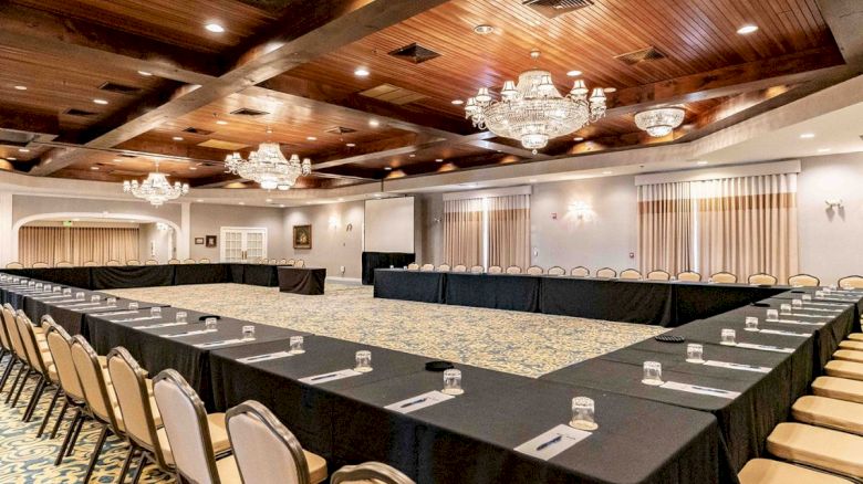 A banquet hall with a large U-shaped table setup, chairs, and chandeliers, ready for a formal event or meeting, with elegant decor and lighting.