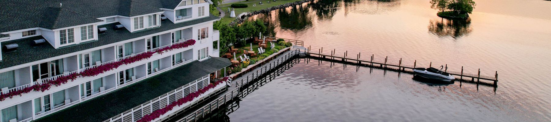 A waterfront building with a dock extending into the water, surrounded by trees and under a sunset sky, can be seen.