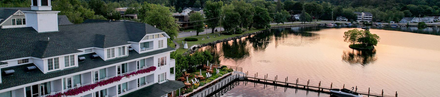 A serene lakeside hotel at sunset with a dock extending into the water, surrounded by lush greenery and a picturesque sky reflecting on the lake.