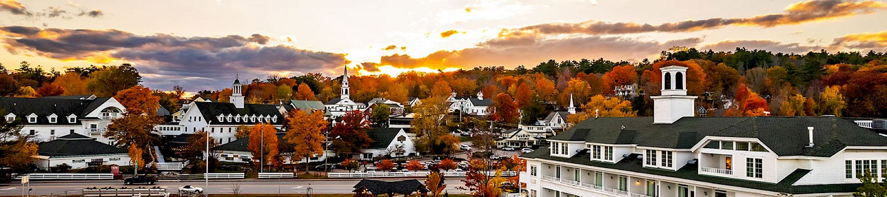 A picturesque lakeside village during autumn, featuring charming white buildings, colorful fall trees, and a serene waterfront at sunset.