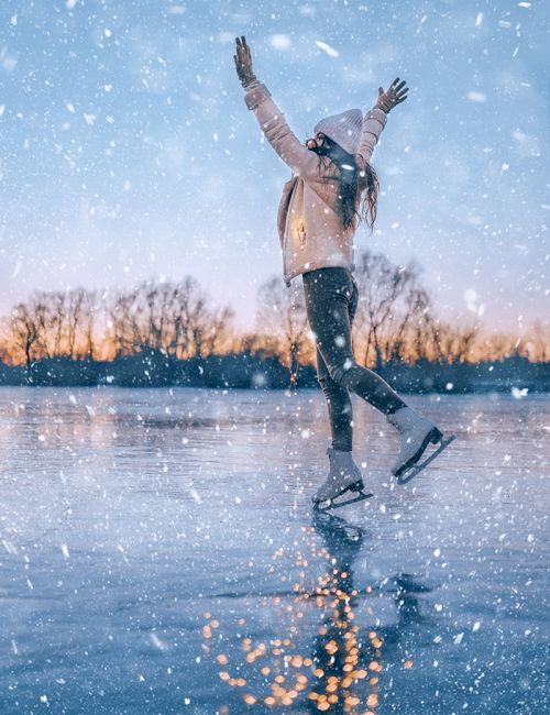 A person ice skating on a frozen lake during snowfall, reaching upwards, as the sunset casts a warm glow in the background.