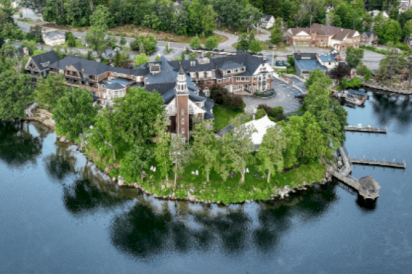 An aerial view of a lakeside estate with a large building, trees, a dock, and surrounding water, likely a resort or institutional facility.