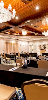 A conference room with rows of tables and chairs, chandeliers, a projector screen, and a wooden ceiling, ready for a meeting or event.