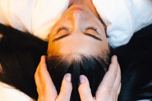 A person with closed eyes is lying down while someone else gently holds their head, possibly in a relaxation or massage setting.