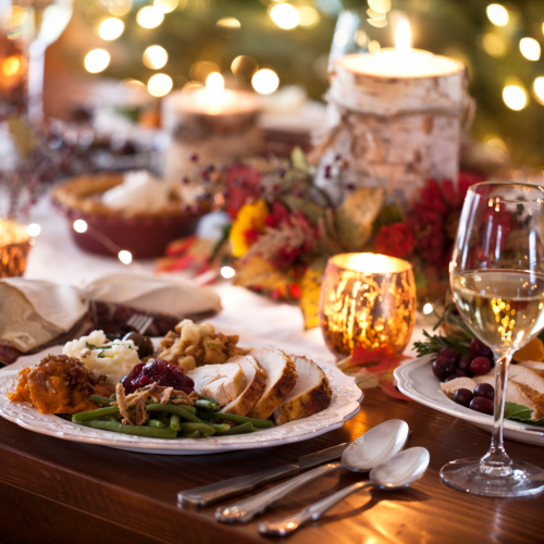 A festive dinner table with plates of food, candles, wine glasses, and holiday decorations, creating a warm and inviting atmosphere.