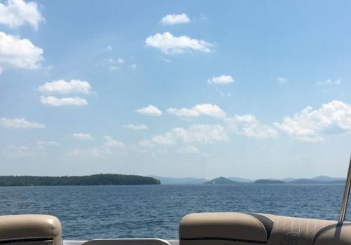 The image shows a serene lake view with scattered clouds in the sky, seen from the seating area of a boat, with islands in the distance.