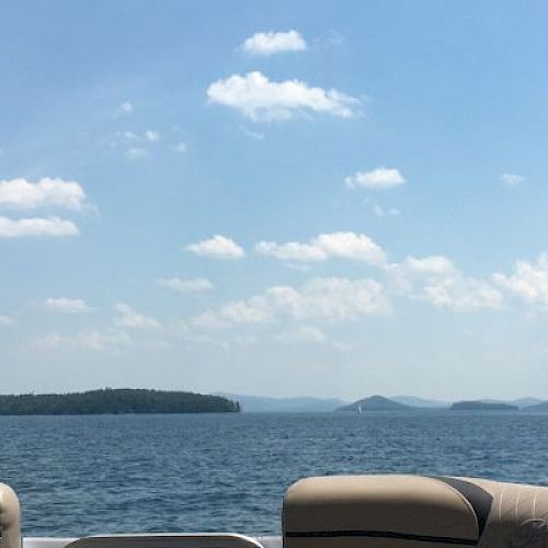 The image shows a serene lake view with scattered clouds in the sky, seen from the seating area of a boat, with islands in the distance.