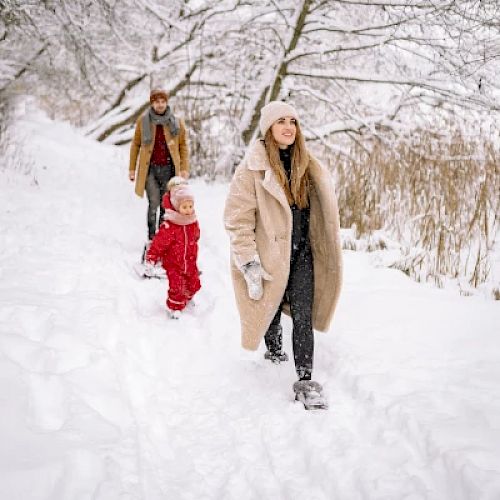 A family walks through a snowy path, bundled up in warm clothing.