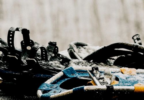 The image shows a set of snowshoes with straps lying on a snowy surface, ready for use in snow-covered terrain.