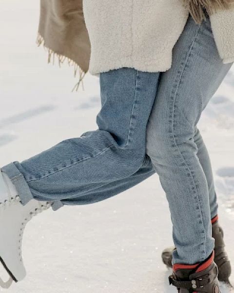 Two people are standing on ice; one person is wearing ice skates while the other person is wearing boots, both are dressed warmly.