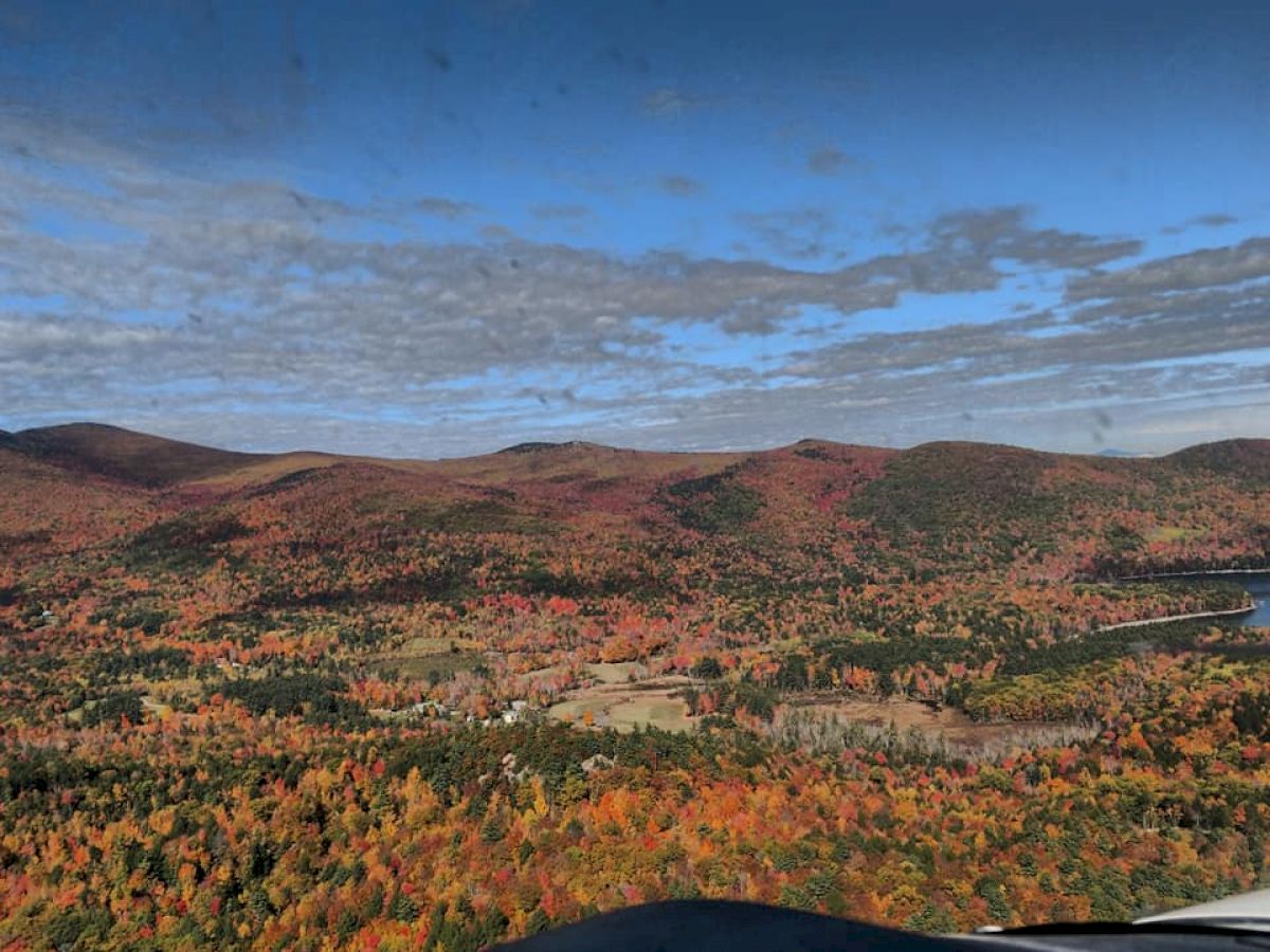 An aerial view of an autumn landscape with rolling hills and vibrant fall foliage under a partly cloudy sky, highlighting the natural beauty.