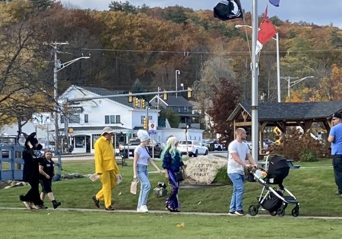 A group of people in costumes walking down a grassy path, with a small town and autumn trees in the background.