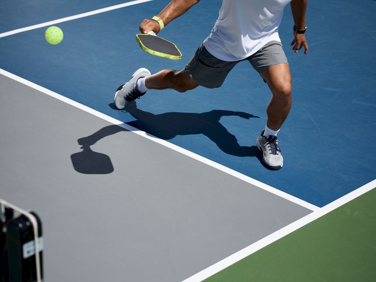 A person is playing pickleball, swinging a paddle to hit a ball on a court. The scene captures dynamic movement and sporty gear.