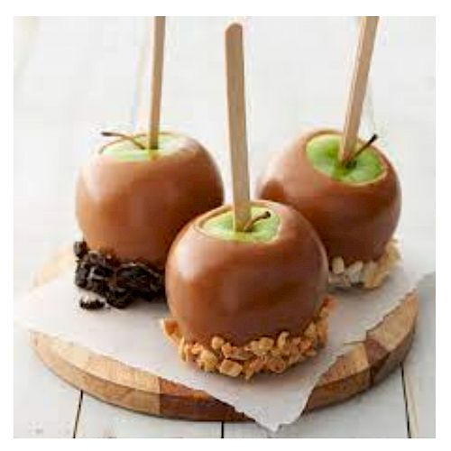 The image shows caramel apples on sticks, with toppings like nuts and cookie crumbs, placed on a wooden board.