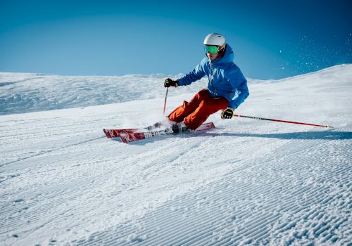 A skier in colorful gear is making a sharp turn on a sunny, snowy slope under a clear blue sky.