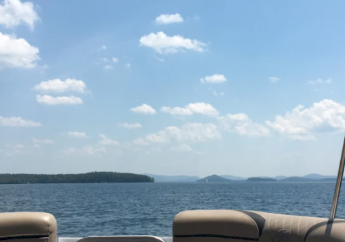 The image shows a view from a boat with a calm lake, distant islands, and a clear, partly cloudy sky.