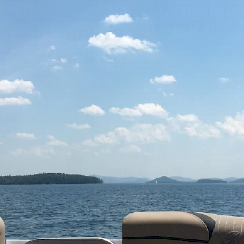 The image shows a view from a boat with a calm lake, distant islands, and a clear, partly cloudy sky.