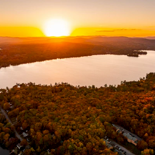 A scenic sunset over a lake surrounded by a forest with vibrant autumn foliage, creating a picturesque and serene landscape.