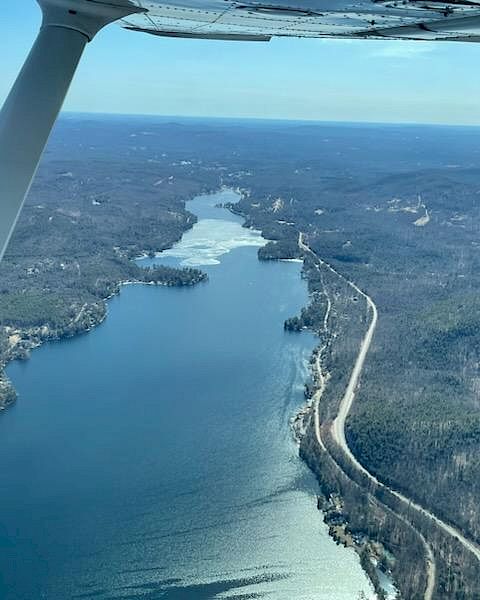 Aerial view of a winding river or lake surrounded by forested landscape with a road running alongside, seen from an airplane in flight.