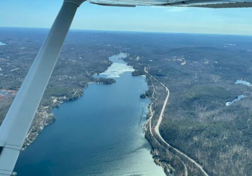 Aerial view of a winding river or lake surrounded by forested landscape with a road running alongside, seen from an airplane in flight.