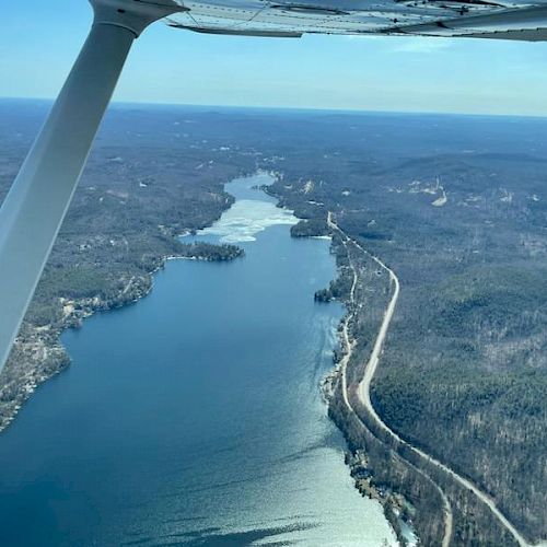 Aerial view of a winding river or lake surrounded by forested landscape with a road running alongside, seen from an airplane in flight.