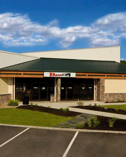 A small building with a green roof and stone facade stands in a parking lot, with clear skies in the background.