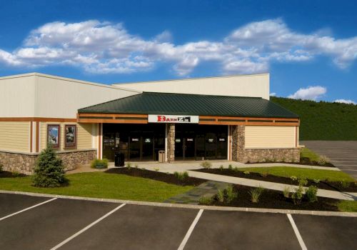 A small building with a green roof and stone facade stands in a parking lot, with clear skies in the background.