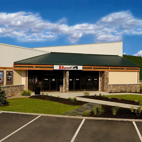 A small building with a green roof and stone facade stands in a parking lot, with clear skies in the background.